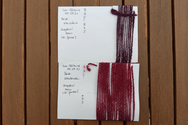 zwei Karteikarten mit aufgewickelter Wolle in zwei verschiedenen Rottönen aus einer Lac-Färbung
