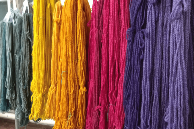 Bunte Stränge mit Naturfarben gefärber Wolle in lila, rot, orange, gelb und grün hängen an einer Kleiderstange zum Trocknen