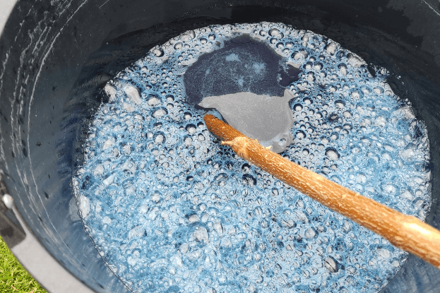 Blaue indigohaltige Flüssigkeit nach Fermentation in einem Eimer, wird mit einem Stock schaumig gerührt