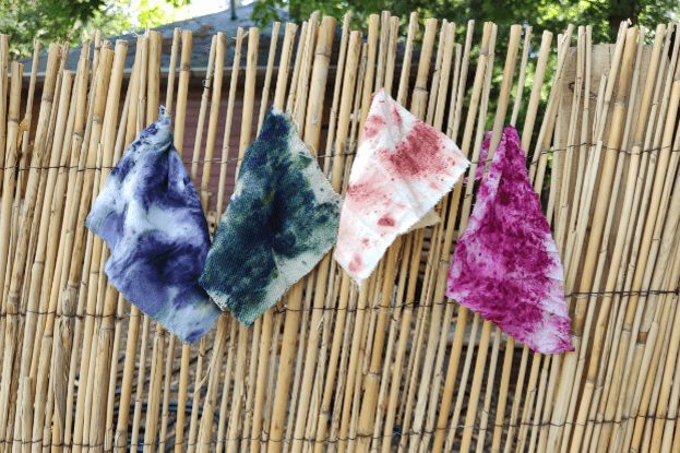 Stoffstücke, die mit Bundle-Dye-Technik gefärbt wurden, hängen an einem Bambusmattenzaun