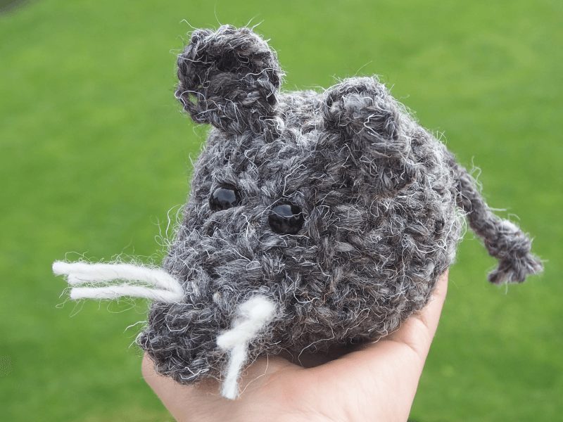 eine nadelgebundene Maus aus dunkelgrauer Wolle sitzt auf einer Hand. sie füllt die Handfläche komplett aus.