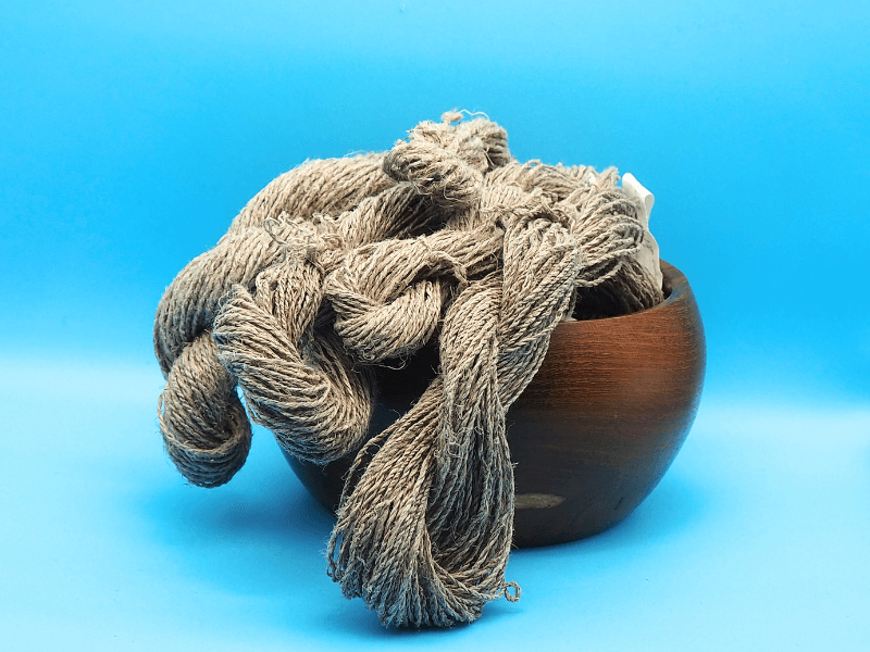 Alle Garne von 1qm Lein 2025 als Stränge in einer Holzschale, sie fallen aus der Schüssel heraus. Hintergrund hellblau.