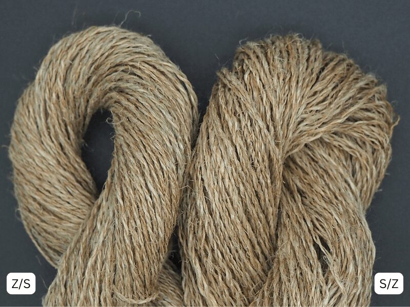Nahaufnahme Langflachsgarne. Links Z/S gesponnen, rechts S/Z gesponnen. Hintergrund schwarz.