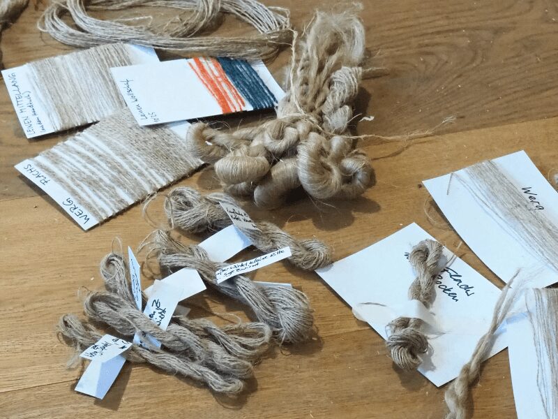 Spinnproben eines Flachskurses liegen auf Pappkarten gewickelt und beschriftet auf einem Holzfußboden.