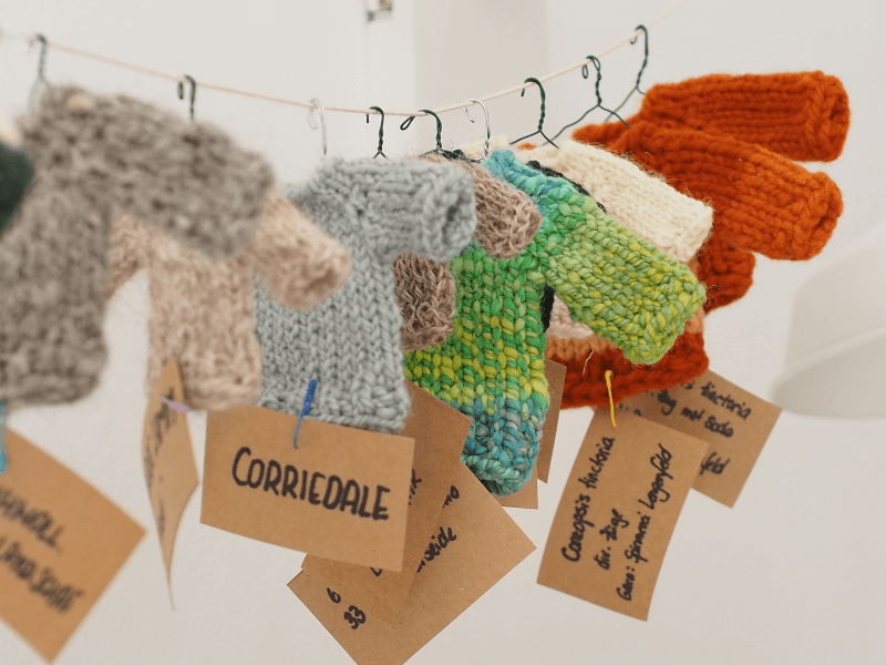 Kleine bunte Mini-Pullover aus handgesponnener Wolle hängen auf Mini-Kleiderbügeln auf einer Schnur.