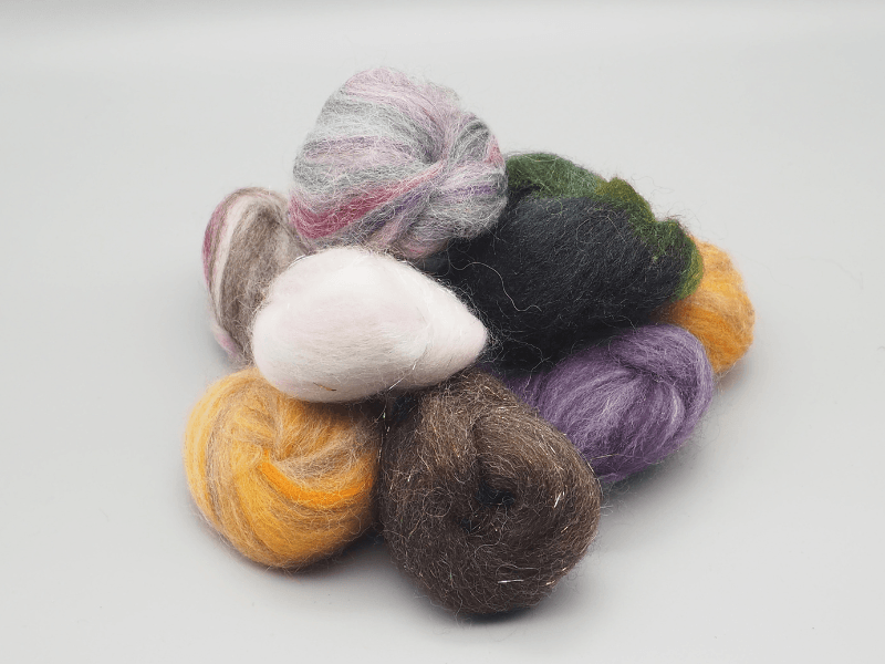 Kleine bunte Faserbällchen in lila, grün, gelb und grau-pink in Nahaufnahme, genannt Spinnkonfekt.
