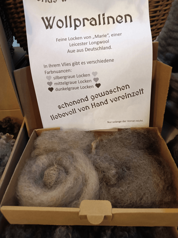 Nahaufnahme einer Schachtel Wollpralinen (hellgraue und dunkelgraue Fasern. Ein Schild erklärt die Herkunft von einer Leicester Longwool Aue.