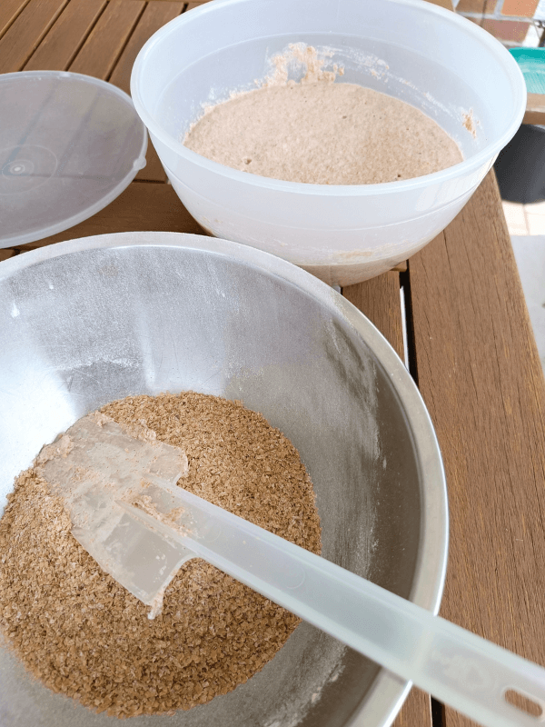 Eine Schüssel mit Weizenkleie und eine mit Sauerteig stehen auf einem Holzlattentisch.